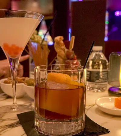 Cocktails served on a marble table with dim lighting and a water bottle in a cozy bar setting.