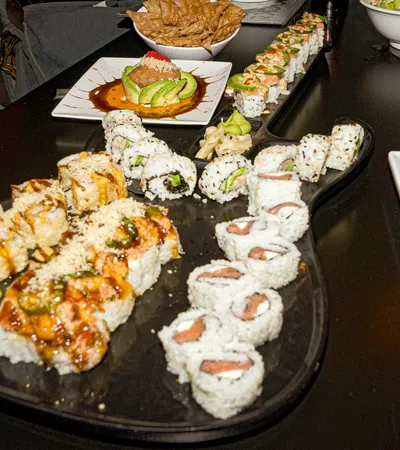 Assorted sushi rolls with sauces and garnishes served on a black platter and white plates on a dark table.