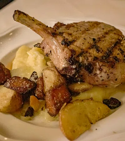 Grilled pork chop served with mashed potatoes and roasted vegetables on a white plate