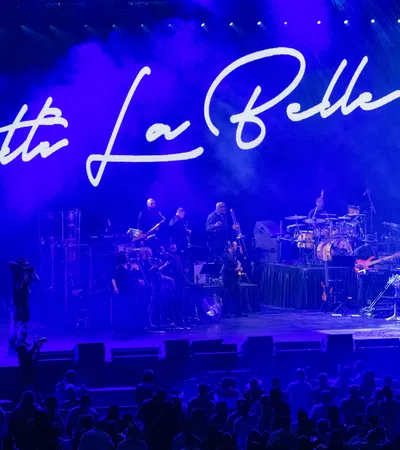 Patti LaBelle performing live on stage with band and blue lighting, audience visible in front of the stage