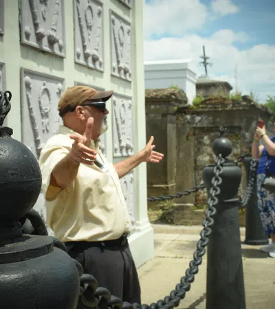 Tour guide explaining historic site details to group of visitors on sunny day outdoors.