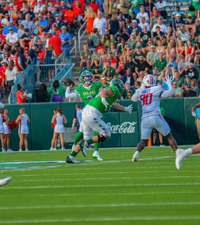 Tulane quarterback prepares to throw under pressure from defenders with crowd and cheerleaders in background