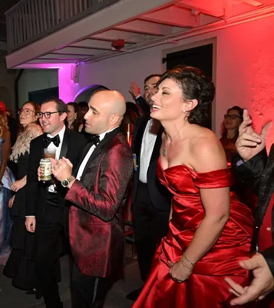 Guests dressed in formal attire enjoy a lively evening party with colorful lighting in an elegant indoor venue.