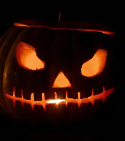 Glowing Halloween jack-o'-lantern with menacing eyes and stitched mouth carved in pumpkin in darkness