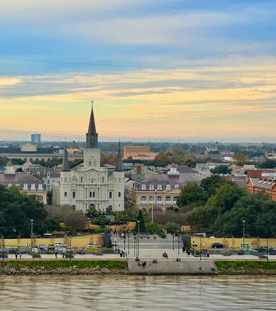 Stunning view of St. Louis Cathedral and Jackson Square with the Mississippi River in the foreground at sunset.