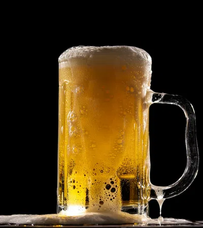 Cold beer mug filled with golden lager and frothy foam against a black background