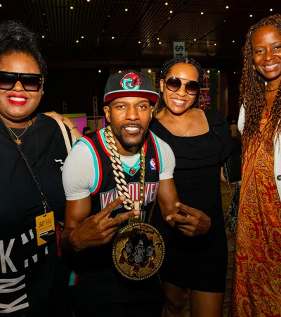 Group of four diverse people smiling at a social event with colorful lighting and casual attire.