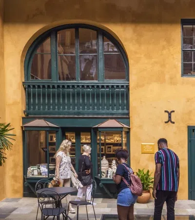 Tourists visiting a yellow stucco building with green doors and windows at a sunny outdoor café seating area.