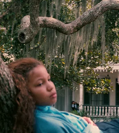 Two women relaxing on large tree branches with a white house and Spanish moss in the background.