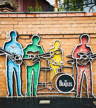 Colorful Beatles band silhouettes mural on brick wall with instruments and drum featuring their band name.