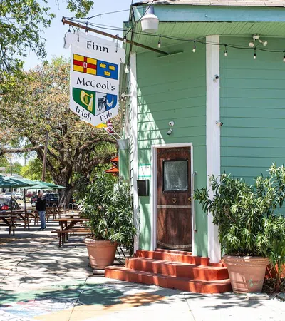 Finn McCool's Irish Pub with green exterior, wooden door, potted plants, and outdoor seating area on a sunny day