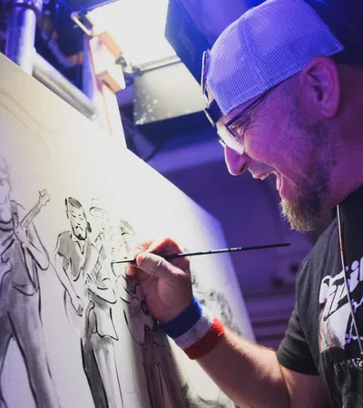 Artist in cap painting a monochrome group portrait on canvas in a studio with focused expression