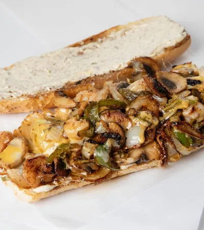 Open shrimp and veggie sandwich with grilled mushrooms, peppers, onions, melted cheese, and creamy spread on white bread.