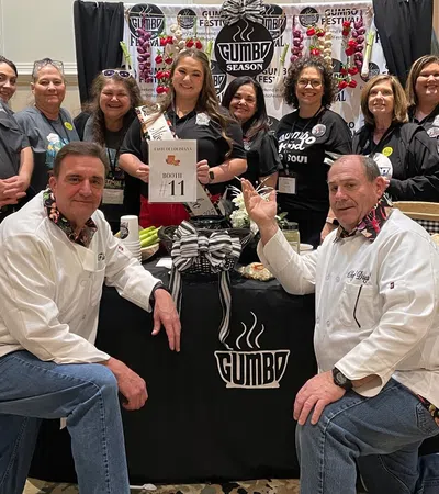 Group of people posing at Gumbo Season Fest booth with festive decorations and promotional materials.