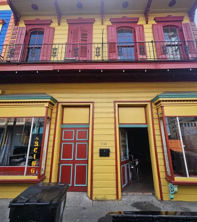 Vibrant yellow and red building with a tattoo and piercing shop, featuring colorful architectural details and balcony.