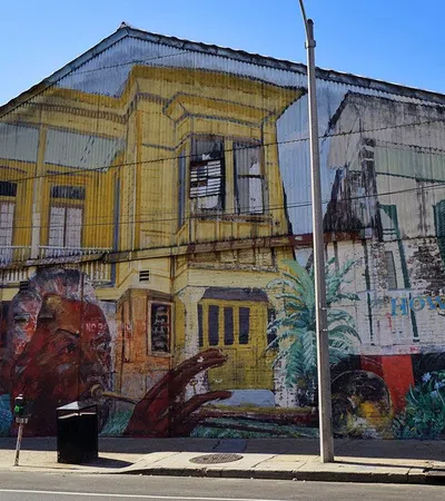 Colorful mural on urban street wall featuring musical instruments, people, and yellow building under clear sky.