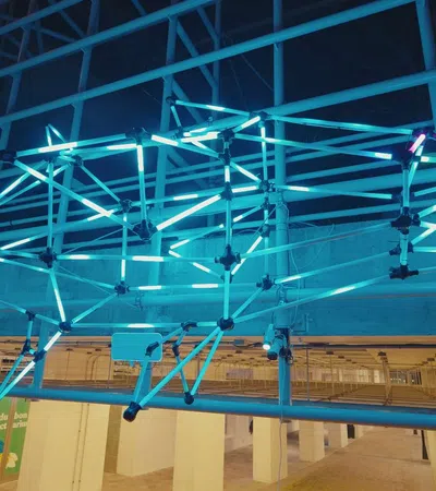 Glowing blue neon light sculpture in the shape of a fish suspended indoors with visible beams and fluorescent tubes.