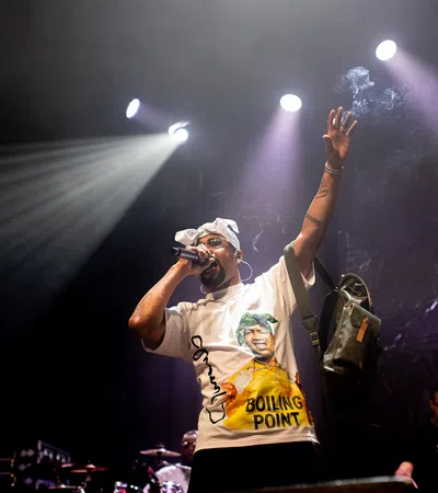 Hip hop artist performing on stage under bright spotlights with microphone and raised arm during concert.