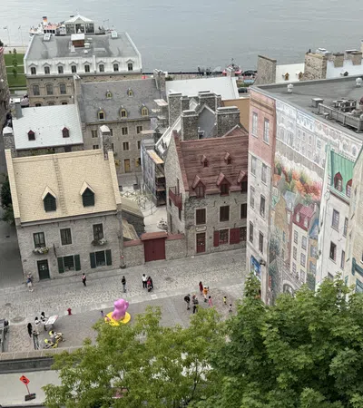 Historic stone buildings and cobblestone streets near waterfront with mural and green trees