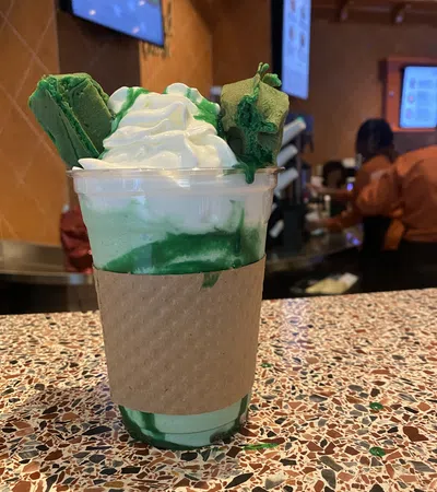 Green matcha frappuccino with whipped cream and green cookies on a speckled countertop in a cafe.