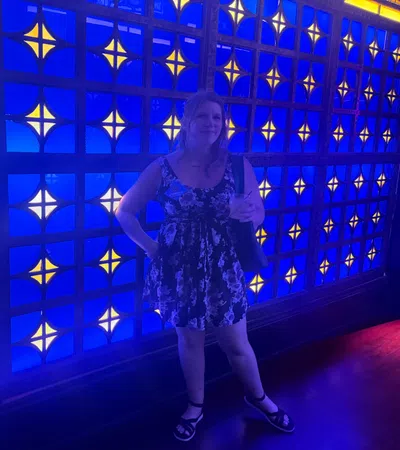 Woman in a floral dress standing in front of a vibrant blue and yellow patterned illuminated wall.