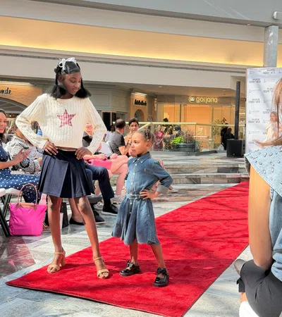 Two young models confidently posing on a red carpet runway during a fashion event in a shopping mall.
