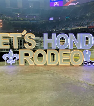 Illuminated sign reading LET'S HONDO RODEO with fleur-de-lis and cowboy boot icons on stadium floor.