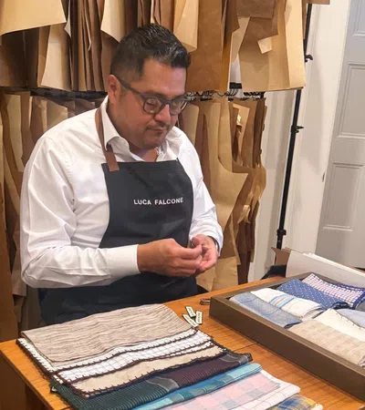 Tailor wearing Luca Falcone apron working with fabric samples in a workshop filled with hanging patterns.