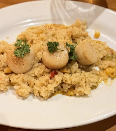 Plate of creamy risotto with three seared scallops and parsley garnish on a rustic wooden table.