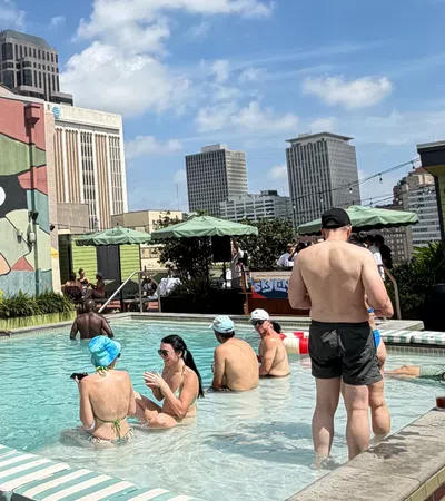 People relaxing and socializing in a rooftop pool with city skyline and colorful mural background on a sunny day.