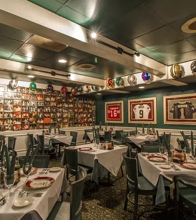 Sports-themed restaurant dining area with framed jerseys, helmets, and photo collage on walls, set tables with plates.