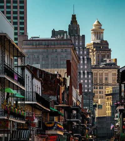 Historic New Orleans street with balconies, colorful decorations, and city skyline in the background under blue sky.