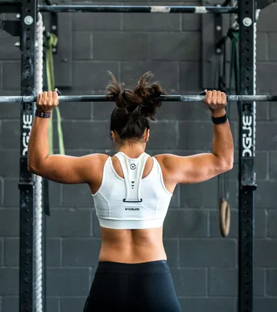 Woman lifting a heavy barbell overhead in a gym with a black brick wall background