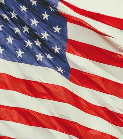 Waving American flag with red and white stripes and white stars on a blue field against sky.