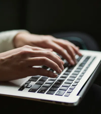 Close-up of hands typing on a laptop keyboard in a dimly lit environment with focused activity.