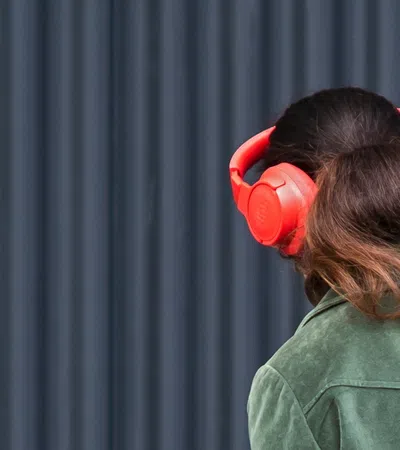 Woman with brown hair wearing a green jacket and bright red over-ear headphones against a dark background