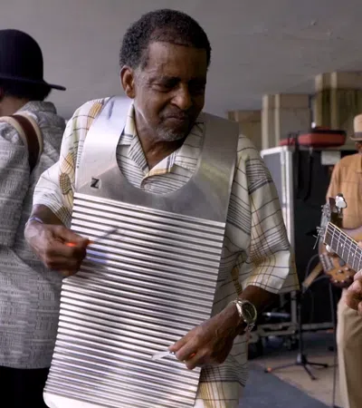 Group of musicians playing guitar, bass, and washboard in a lively outdoor setting.