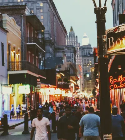 Crowded Bourbon Street in New Orleans at dusk with lit signs and historic buildings lining the street