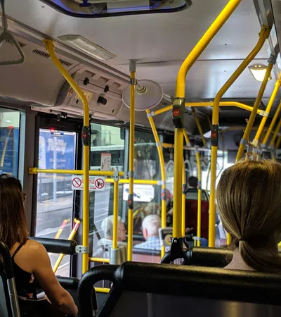 Passengers seated inside a city bus with yellow handrails and windows showing an urban street outside.