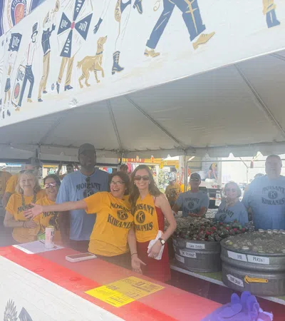 Group of Molsaint Kiwanis volunteers smiling and serving drinks under a festival tent with beer tubs.