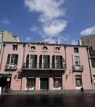 Historic pink building with green shutters and balconies under a blue sky with scattered clouds.