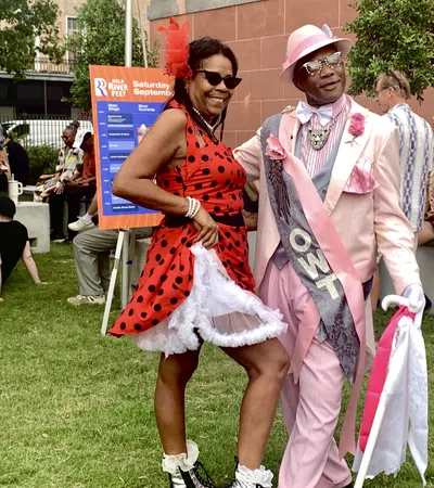 Couple dressed in vibrant retro outfits enjoying an outdoor festival on a sunny day with people relaxing nearby