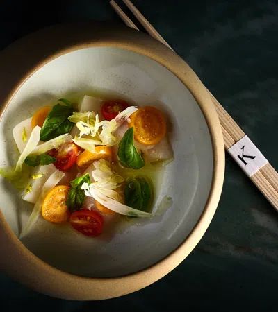 Elegant bowl of fresh vegetable salad with cherry tomatoes, greens, and chopsticks on dark surface.