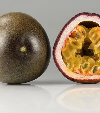 Whole and halved passion fruit showing wrinkled purple skin and juicy yellow seeds inside on a light background.