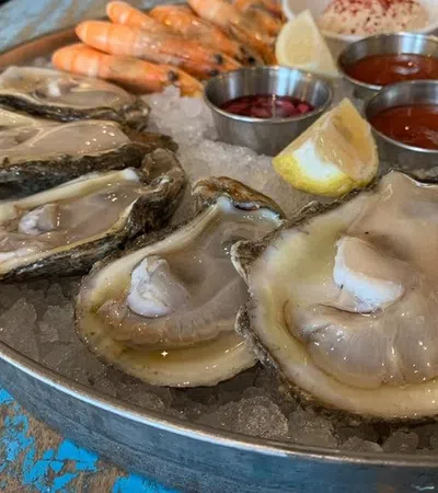 Fresh oysters and shrimp on ice with lemon wedges and dipping sauces on a metal platter.