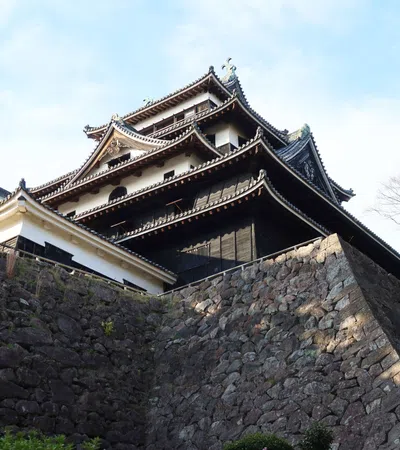 Traditional Japanese castle with multi-tiered roofs atop large stone walls under a clear sky.