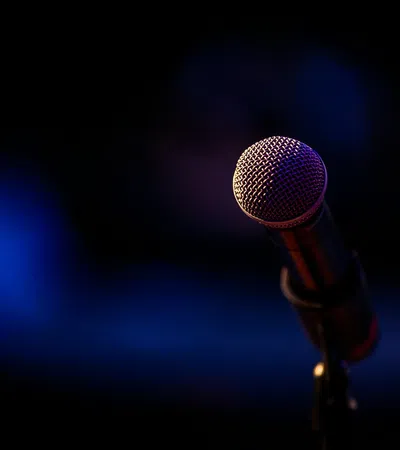 Close-up of a stage microphone with dark blurred background and purple-blue lighting effect.