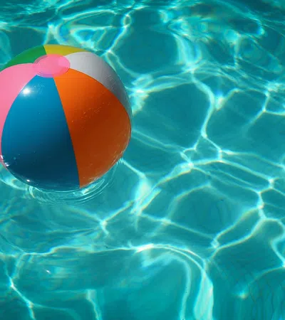 Colorful beach ball floating on the clear blue water surface of a swimming pool with light reflections.