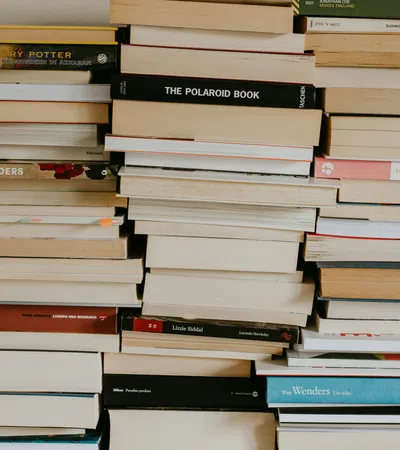 Stacks of assorted books piled horizontally and vertically on a shelf with varied colored covers and spines.