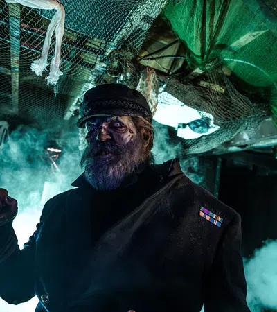 Dark haunted captain with a hook hand and eerie blue lighting in a spooky, fog-filled ship interior.
